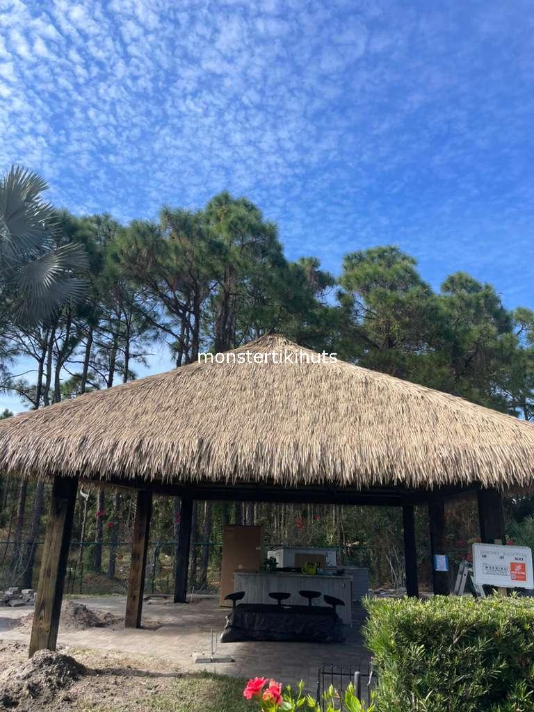 Large tiki hut with synthetic thatch roof in a wooded setting